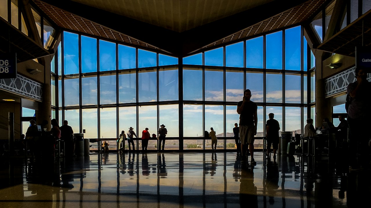Travellers as silhouettes at a tall terminal window at dusk, looking out over the apron