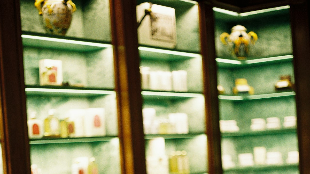 Rows of clear perfume flacons lined up on a counter in front of warm backlit glass shelving